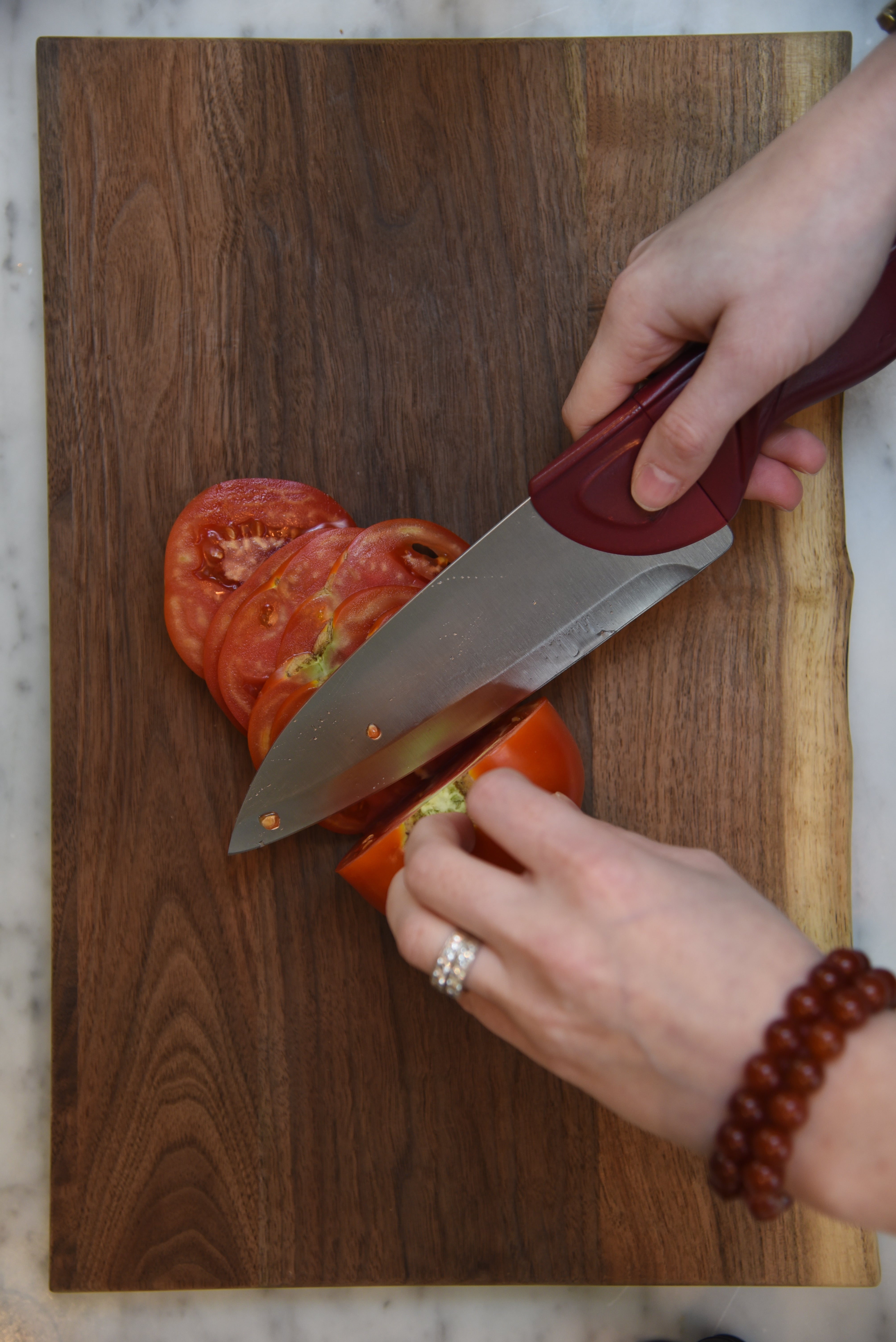 A Cardinal Red Chef Knife Cutting an Heirloom Tomato on Rustic Wood Board on Marble Countertops