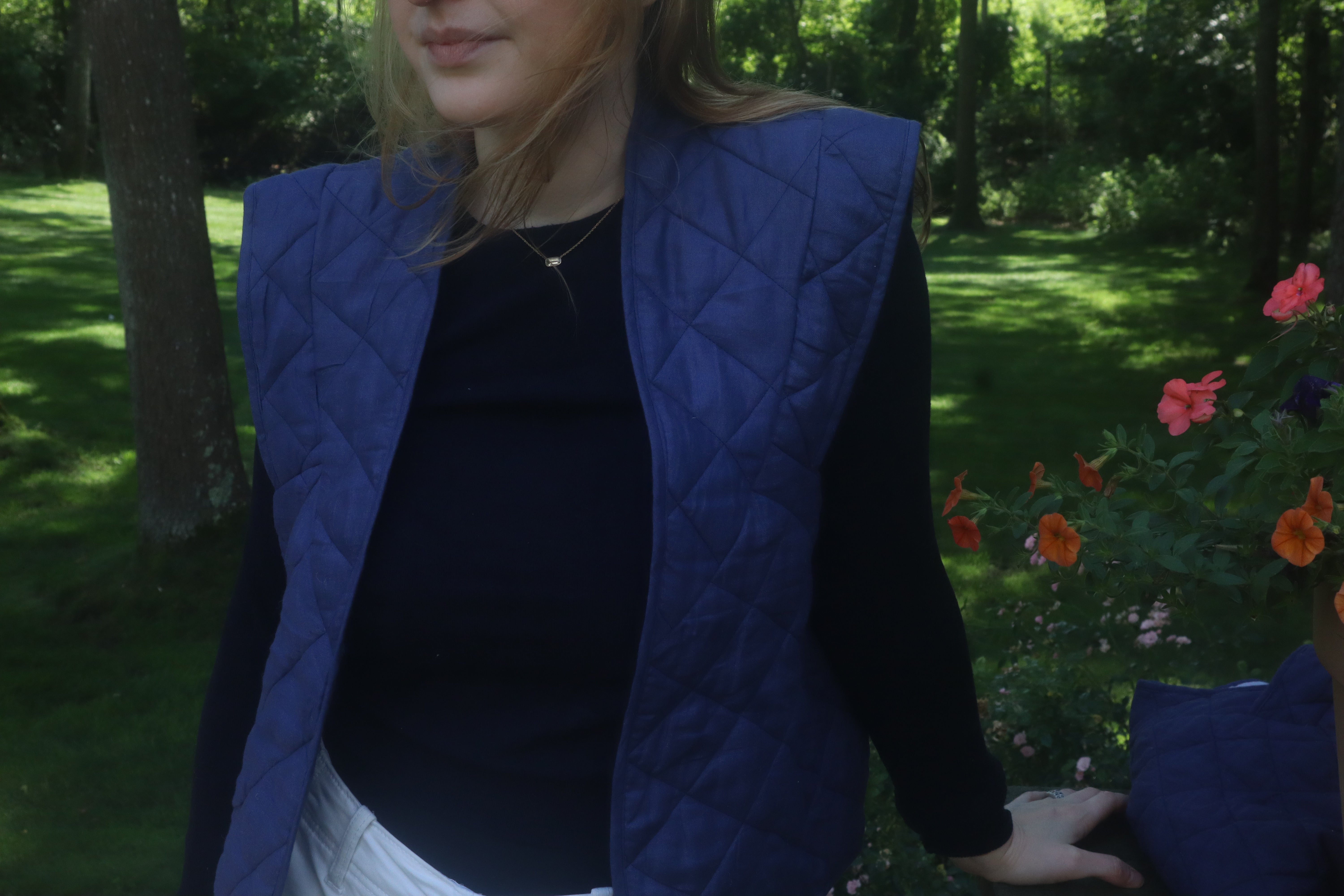 Lightweight Navy Vest for Kitchen use, water repellent, navy closure. Pictured in a lawn grass beautiful and a girl standing in white pants, a navy sweater and a simple necklace