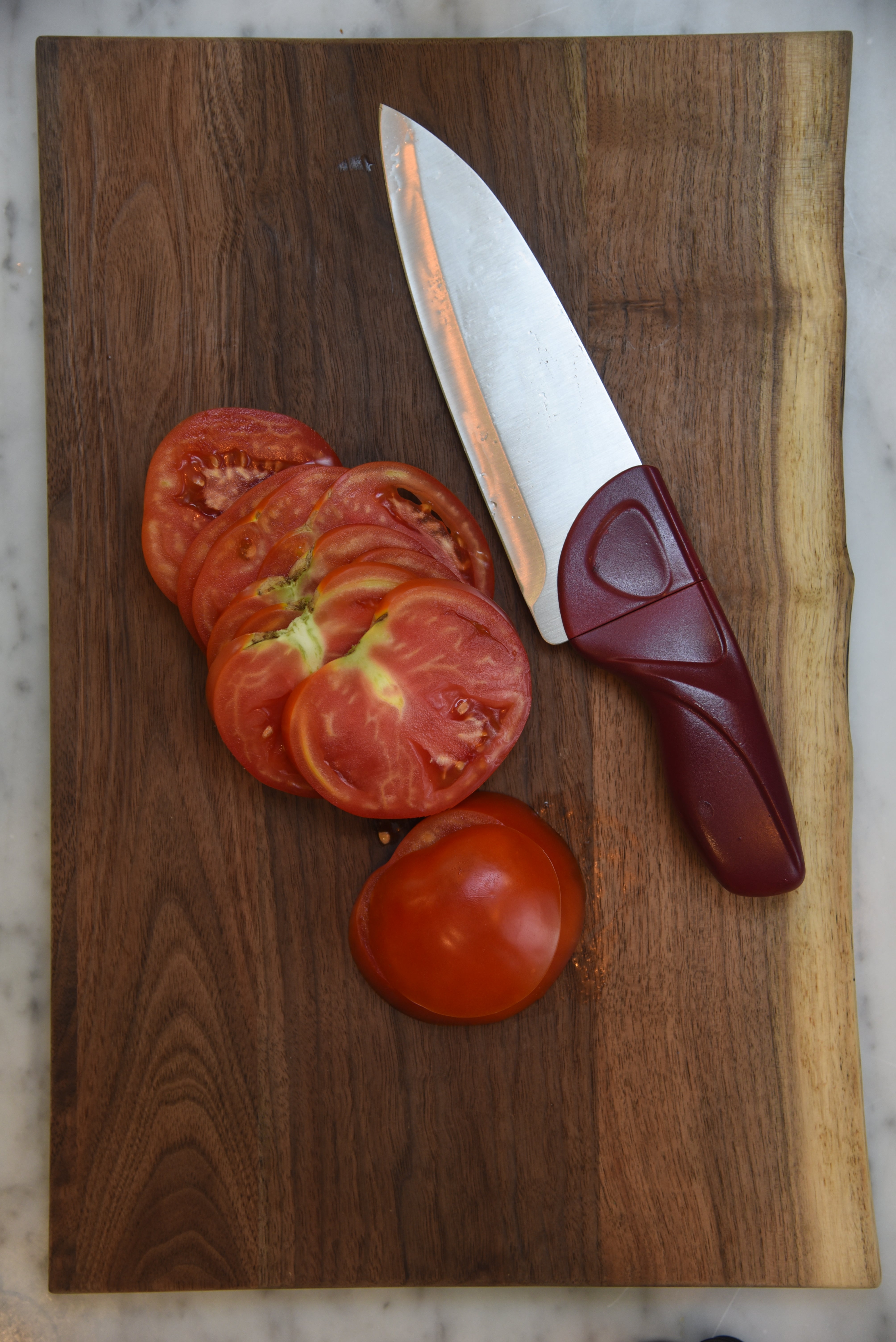 Cardinal Red Chef Knife with Tomatoes and Wood Cutting Board on Marble Counter