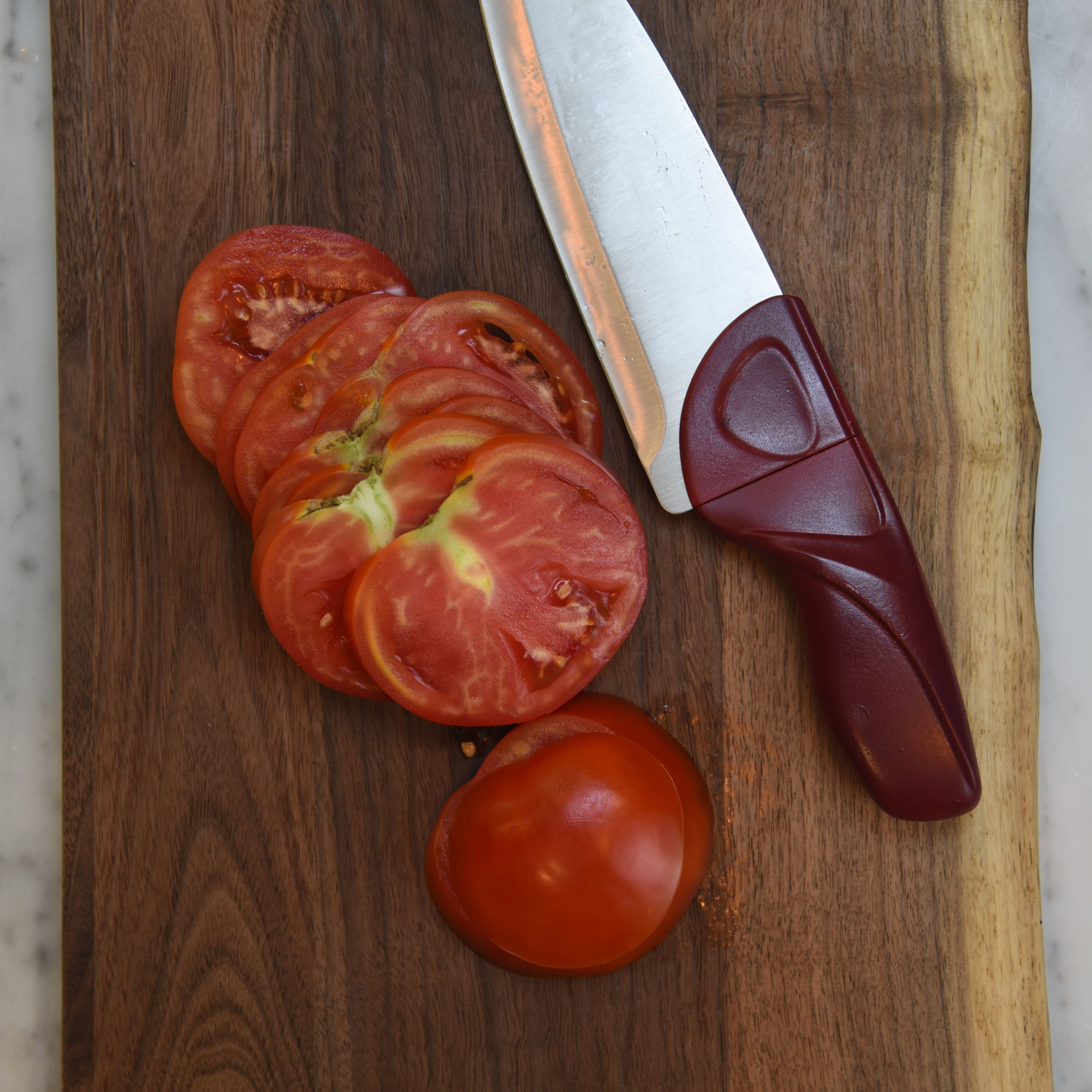 Cardinal Red Chef Knife with Tomatoes and Wood Cutting Board on Marble Counter