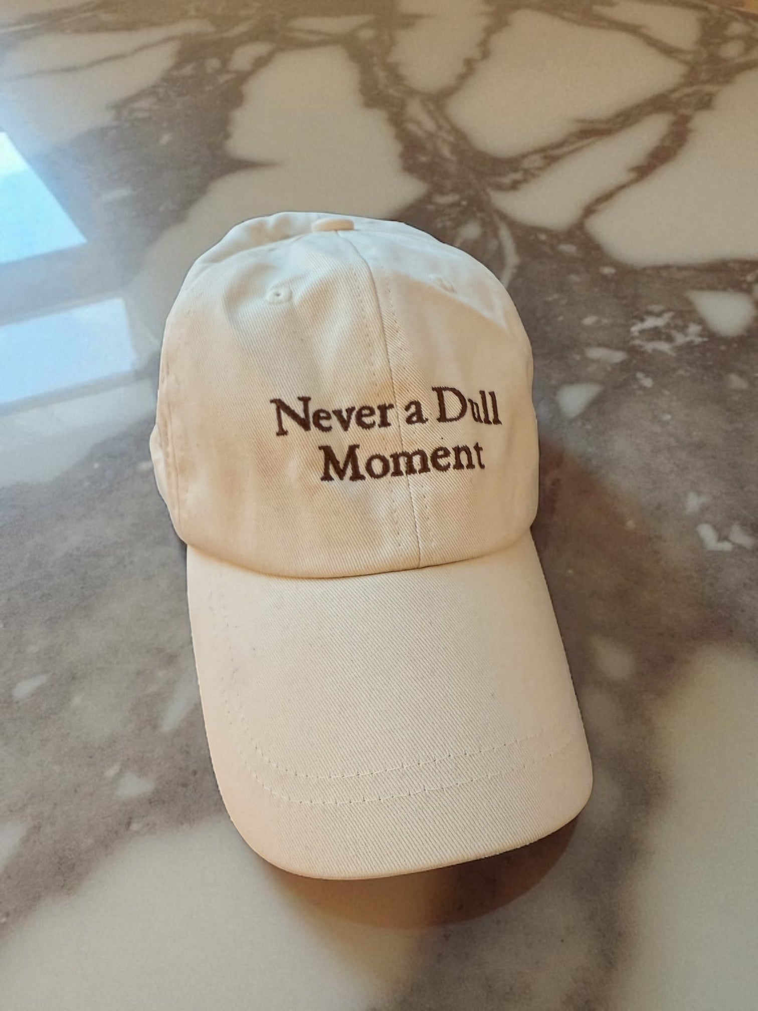 beige canvas baseball hat with brown writing ' never a dull moment' Arabescato brown marble