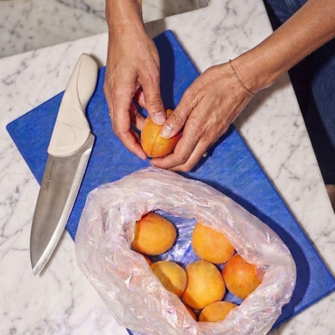 Cream Color Chef Knife woman cutting Apricots on blue cutting board and marble countertop