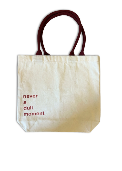 Beige tote bag with red text 'never a dull moment' on a white background