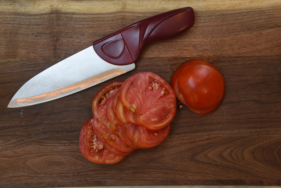 Knife with a maroon handle next to sliced tomatoes on a wooden surface