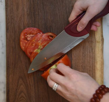 A Cardinal Red Chef Knife Cutting an Heirloom Tomato on Rustic Wood Board on Marble Countertops