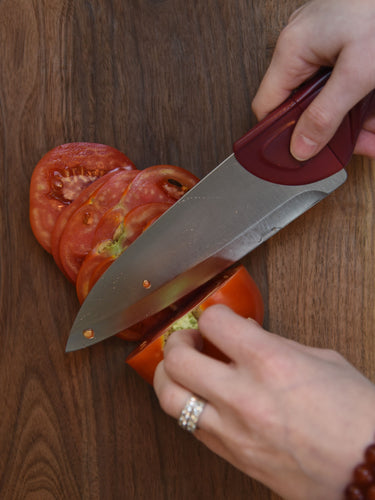 A Cardinal Red Chef Knife Cutting an Heirloom Tomato on Rustic Wood Board on Marble Countertops