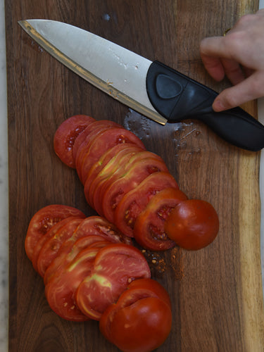 Sliced tomatoes on a wooden cutting board with a knife and a hand holding it.