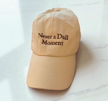 Cream Canvas Baseball hat with brown thread 'never a dull moment' on a countertop