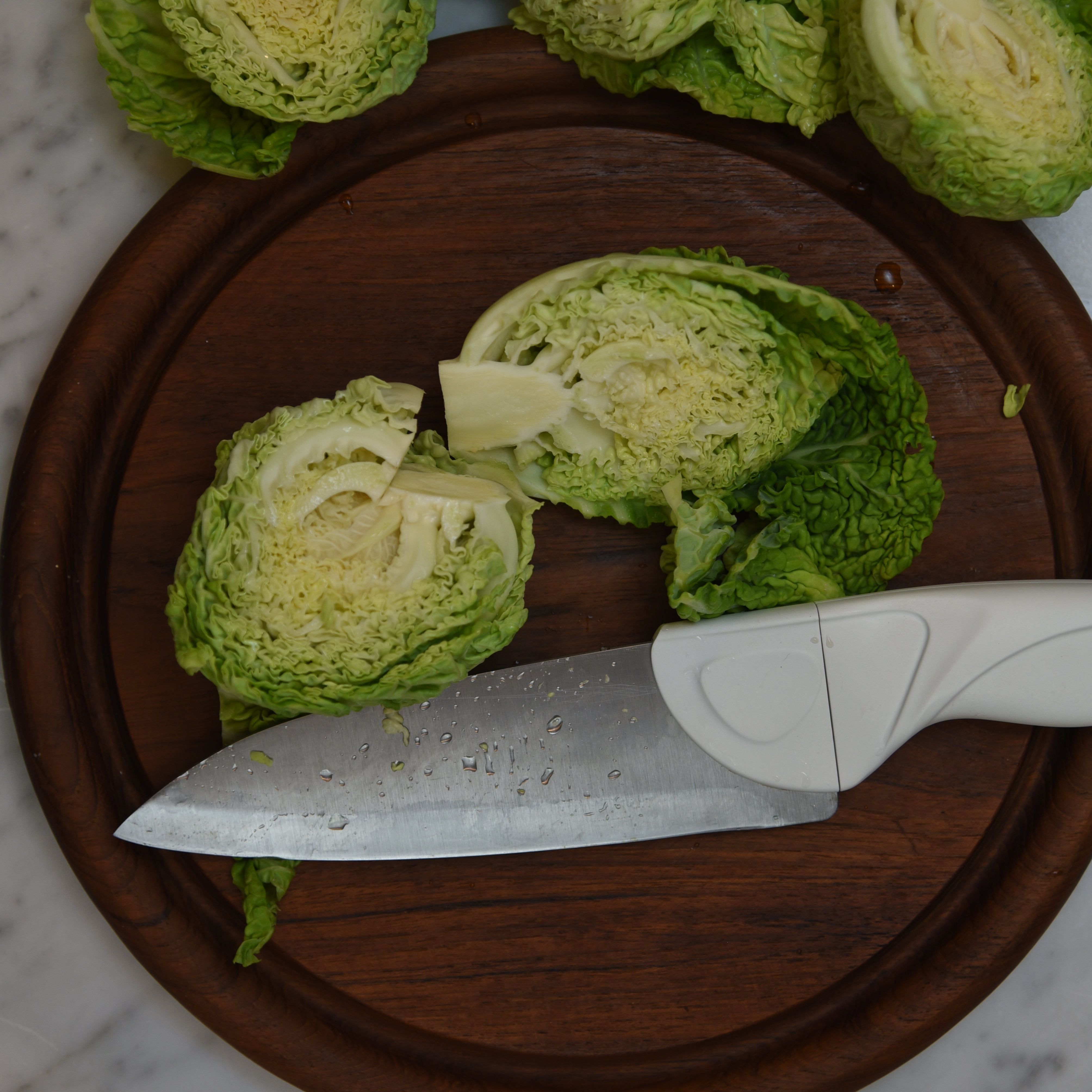 Cream Chef Knife Being cut on round wood cutting board, cutting baby savoy cabbage on marble countertop