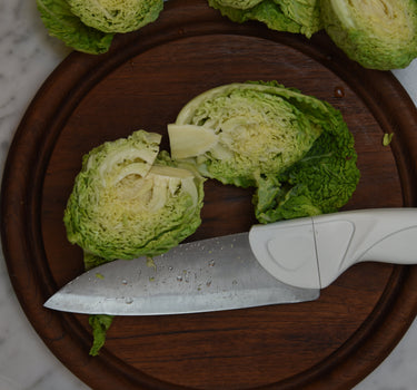 Cream Chef Knife Being cut on round wood cutting board, cutting baby savoy cabbage on marble countertop