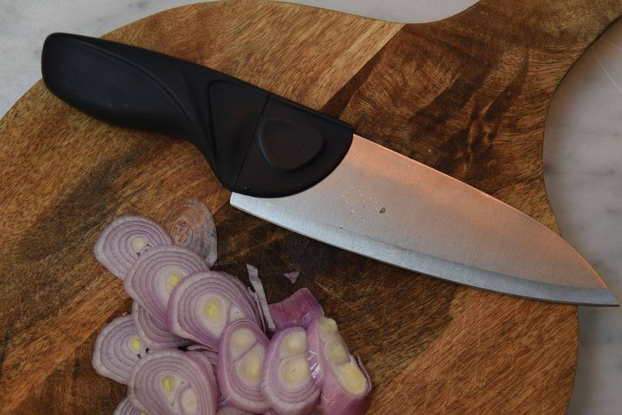Knife with black handle on a wooden cutting board with sliced shallots