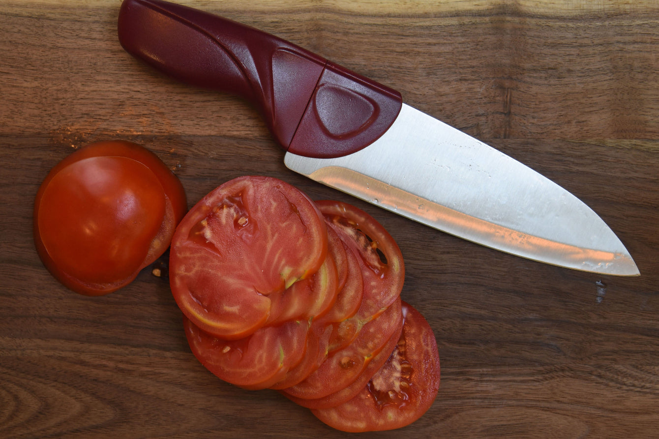 Chef knife with a red handle next to sliced tomatoes on a wooden surface