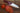 Chef knife with a red handle next to sliced tomatoes on a wooden surface