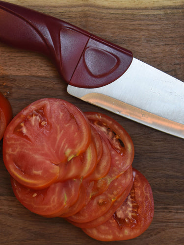 Chef knife with a red handle next to sliced tomatoes on a wooden surface