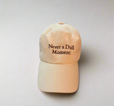 Beige cap with 'Never a Dull Moment' text on a light gray background