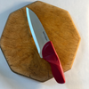 Red-handled knife on a wooden cutting board with a white background