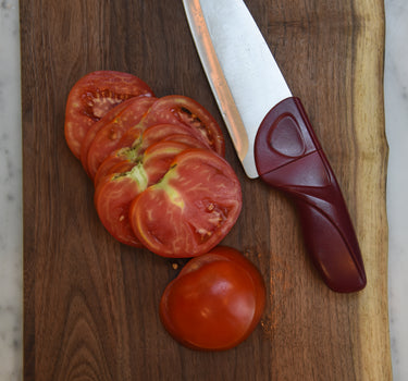Cardinal Red Chef Knife with Tomatoes and Wood Cutting Board on Marble Counter