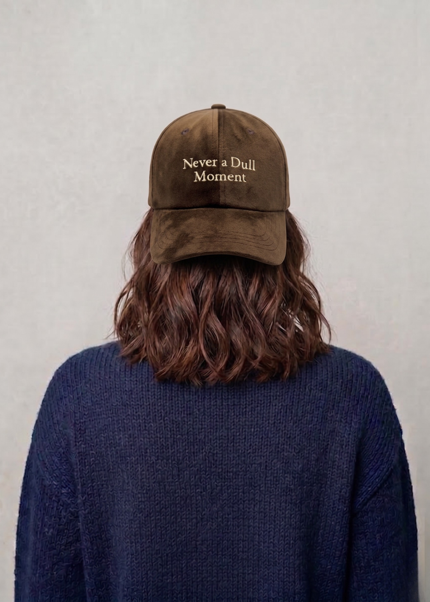 Person wearing a brown cap with 'Never a Dull Moment' text on a plain background