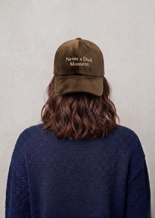 Person wearing a brown cap with 'Never a Dull Moment' text on a plain background