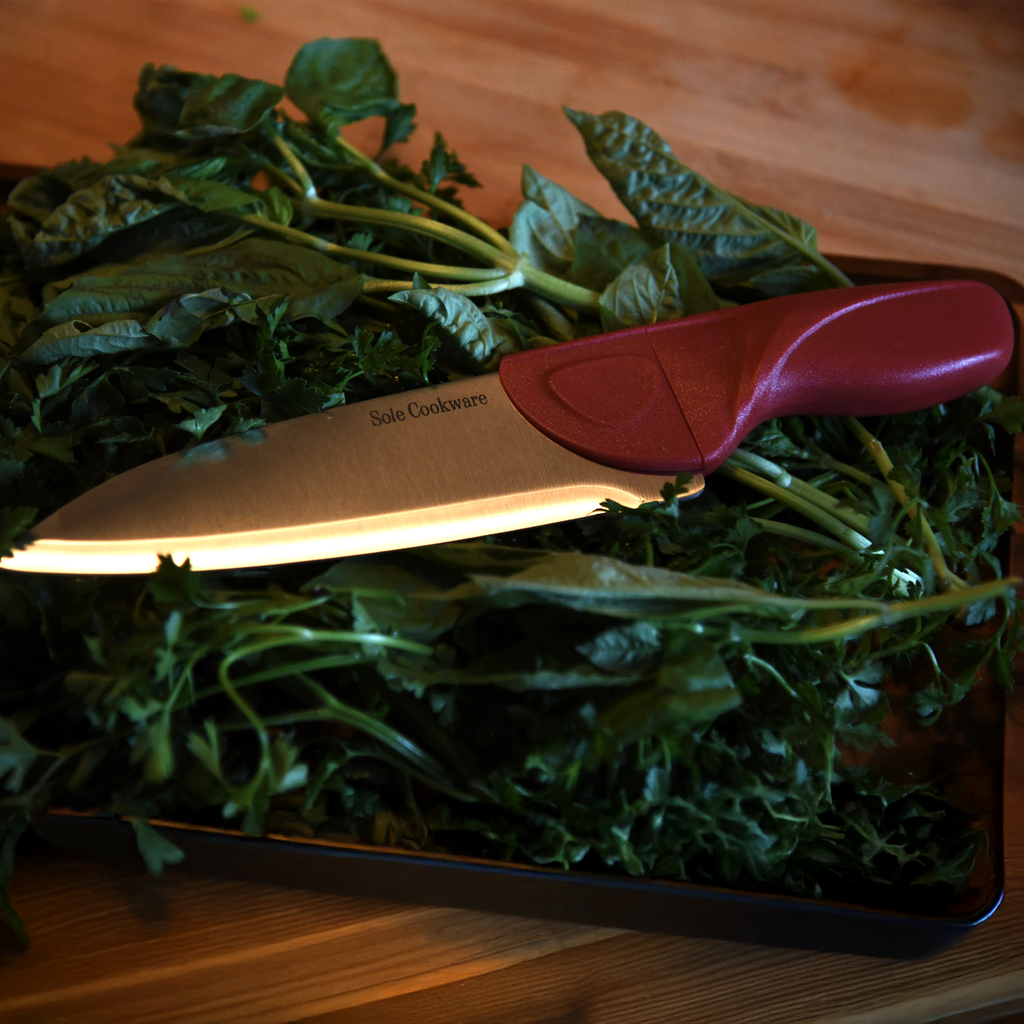 Knife with a red handle on a pile of green leafy vegetables on a wooden surface